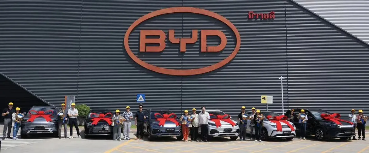 Participantes posam ao lado de veículos BYD decorados com laços vermelhos durante uma cerimônia de entrega fora da fábrica da empresa na Tailândia.