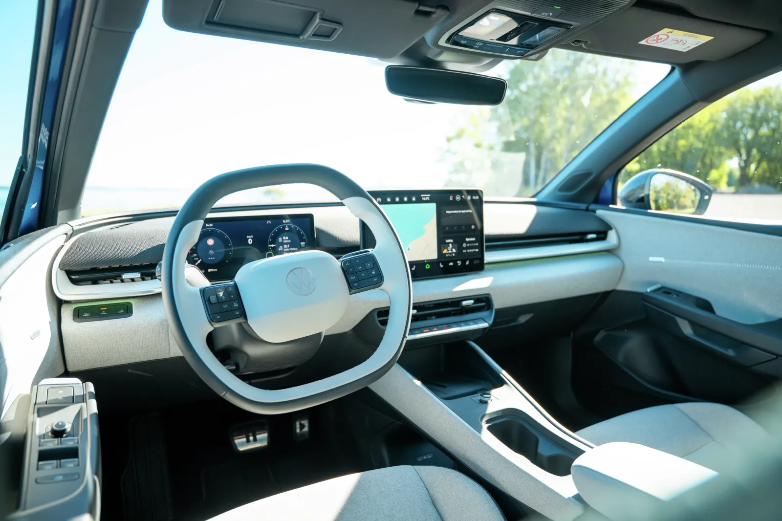 Interior moderno de carro elétrico da Volkswagen com volante semelhante ao de um carro, dois monitores digitais e acabamento cinza claro.