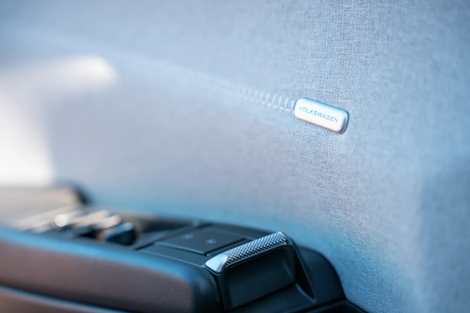 Imagem de close do logotipo da Volkswagen em um painel interno de tecido cinza com botões de controle do ar-condicionado.