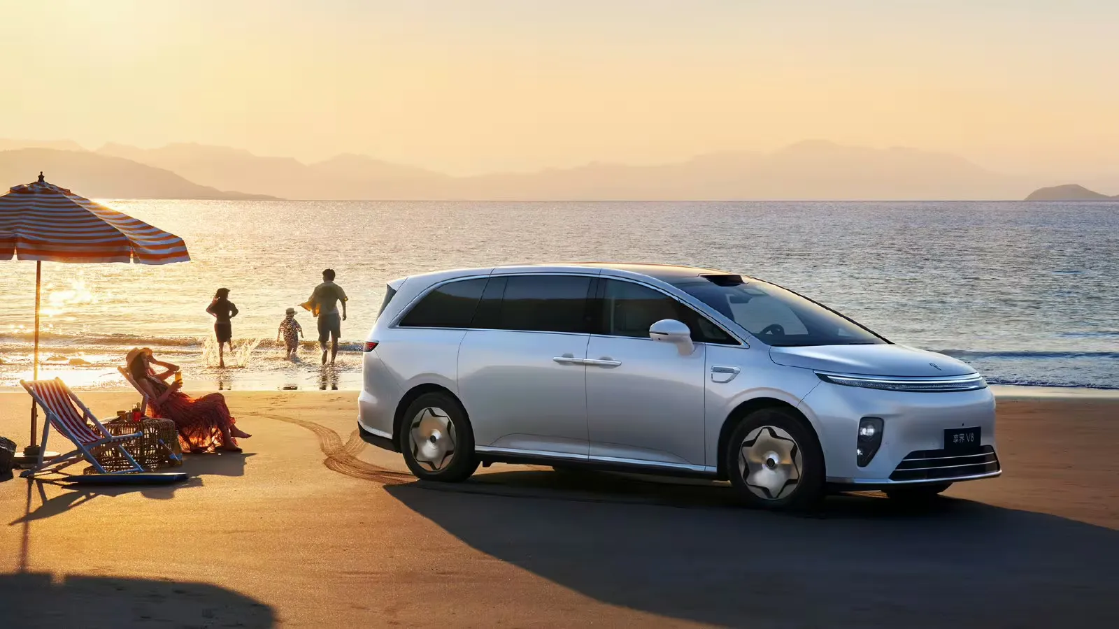 White Stelato V8 MPV parked on a beach at sunset, with a family by the water in the background.