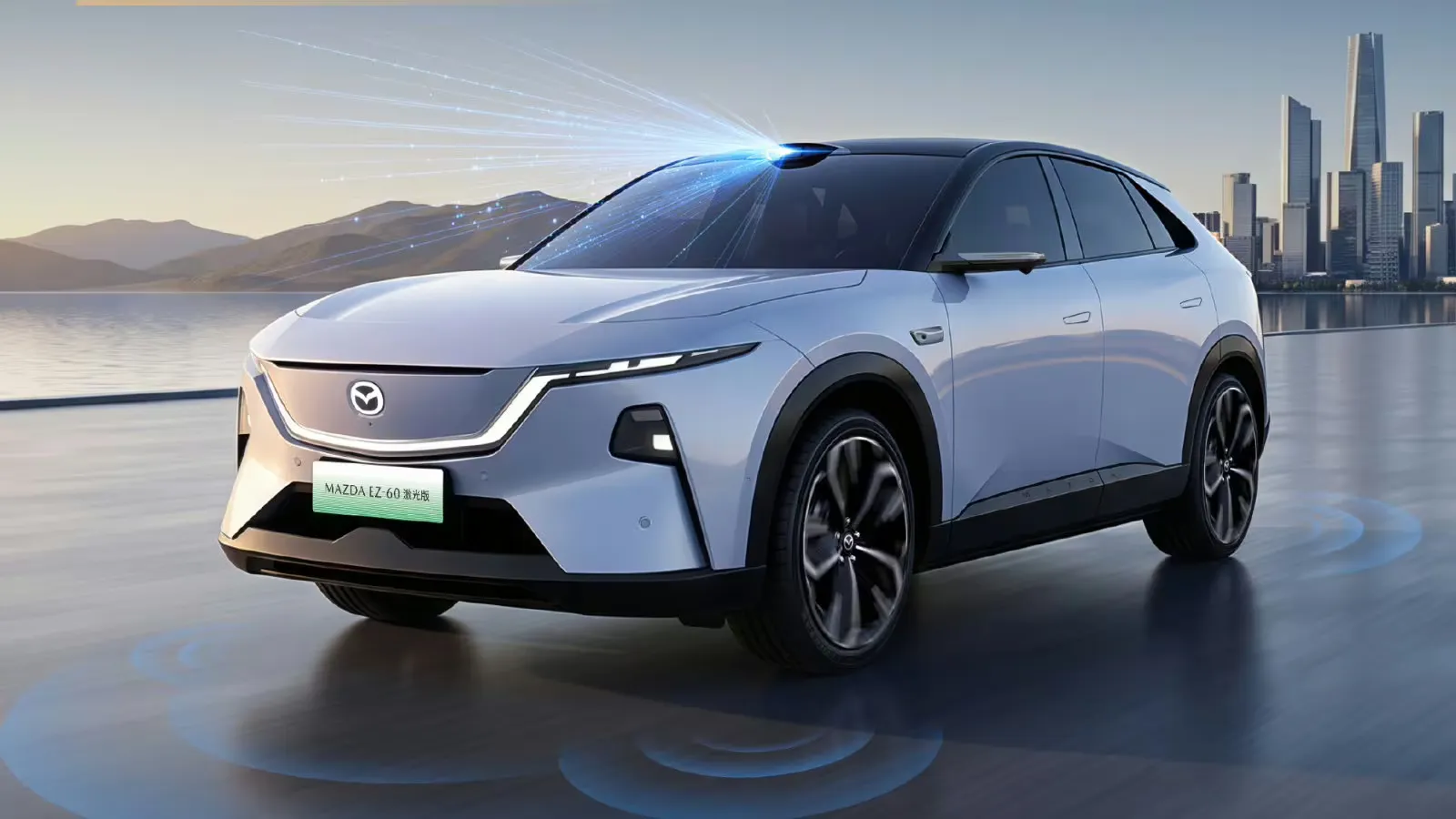 Visão traseira de três quartos de um modelo branco do Mazda EZ-60 com variante LiDAR, equipado com sensor LiDAR montado no teto que emite feixes de luz azul, estacionado em uma estrada à beira-mar com montanhas e o horizonte da cidade ao fundo. Anéis azuis no chão ilustram a área de cobertura dos sensores do veículo.