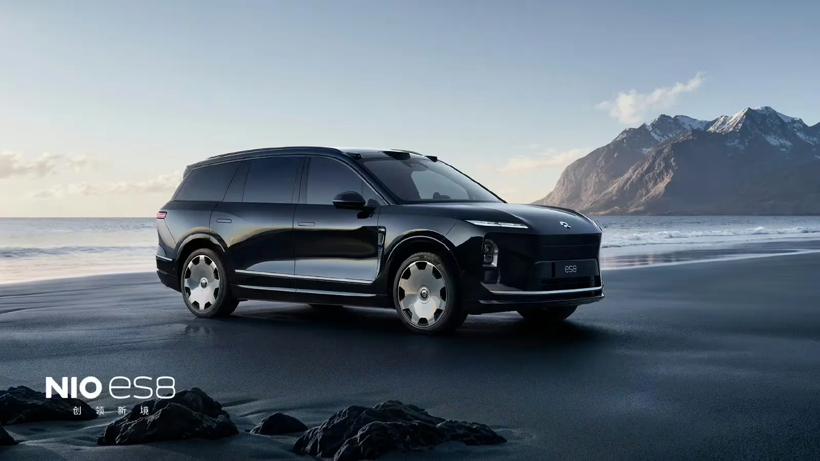 Black Nio ES8 with 22-inch Lanyue forged wheels on a beach, with snow-dusted mountains in the background.