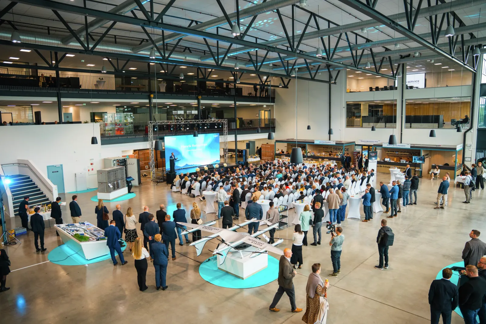 Large indoor business event in a modern industrial hall featuring drone demonstrations, live presentations, stages, and LED screens.