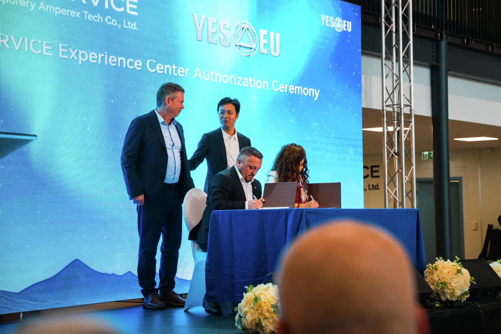 Two men talking at a professional event or conference with a blue sign behind them.