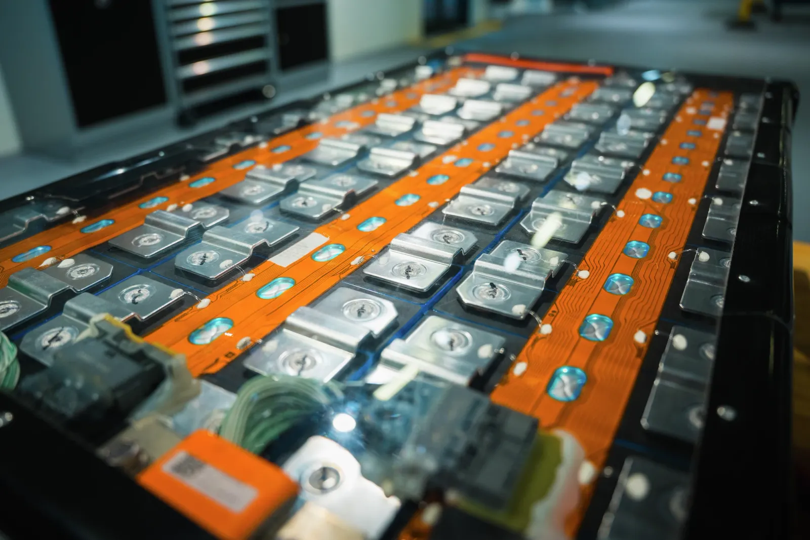 Close-up of a lithium-ion battery pack in an electric vehicle with orange flexible circuit boards and metal cell contacts.
