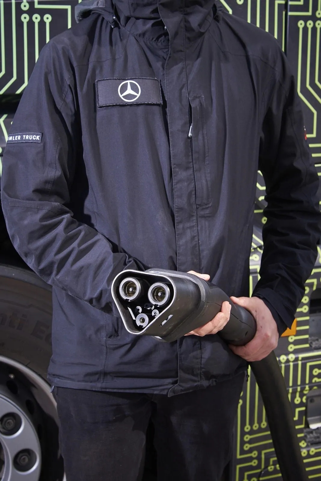 A technician holds an MCS charging connector with its contacts visible.